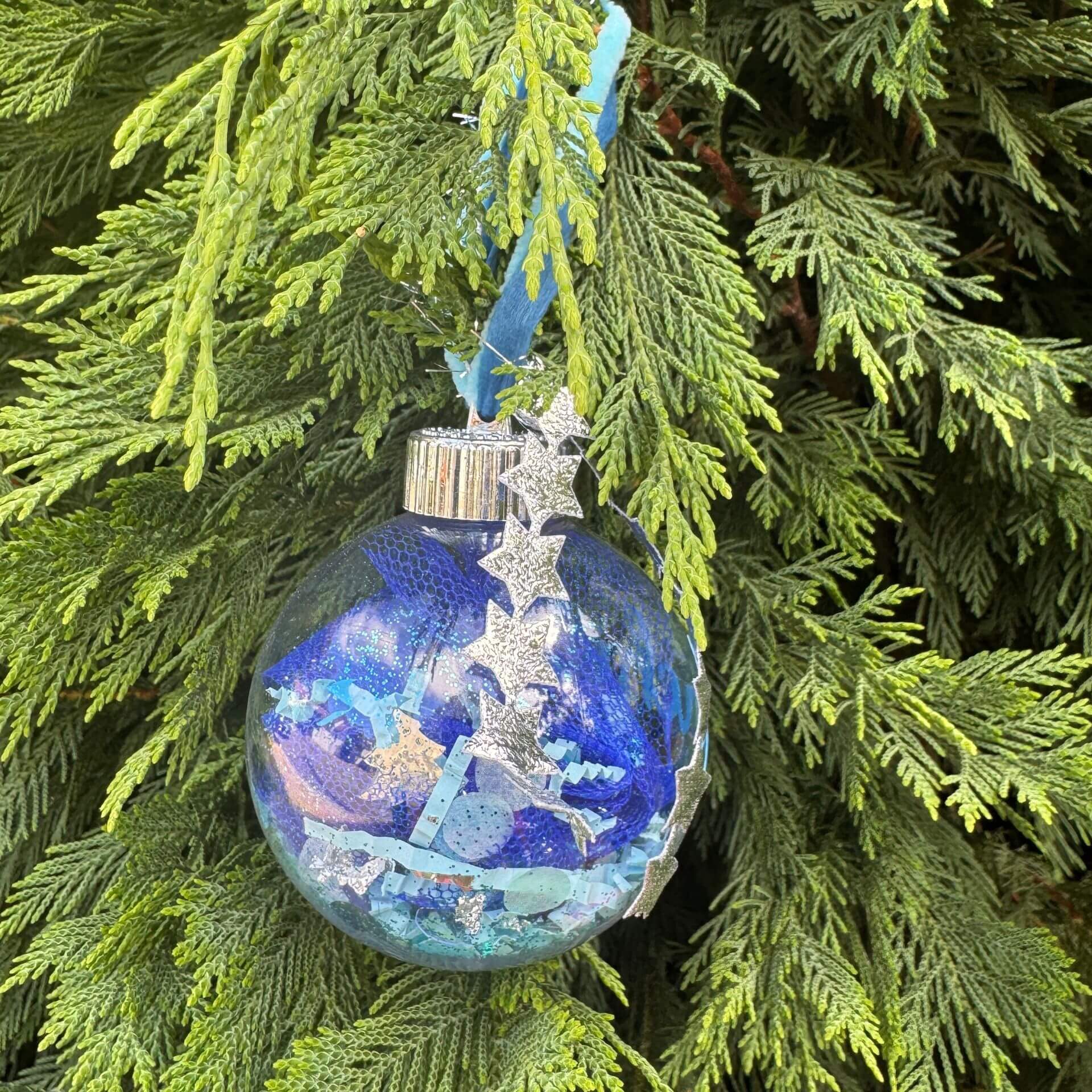 Decorative Christmas ornament with a blue and silver design hanging on a green tree.