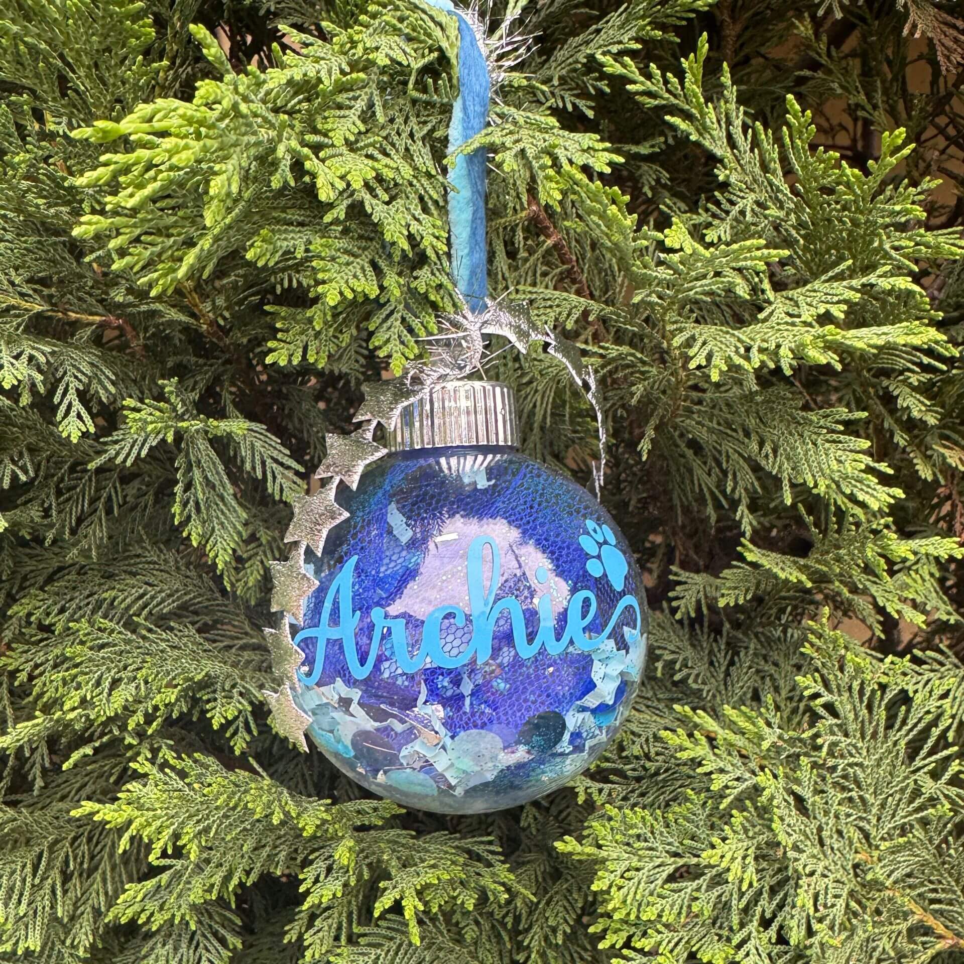 Blue ornament with 'Archie' text hanging on a Christmas tree
