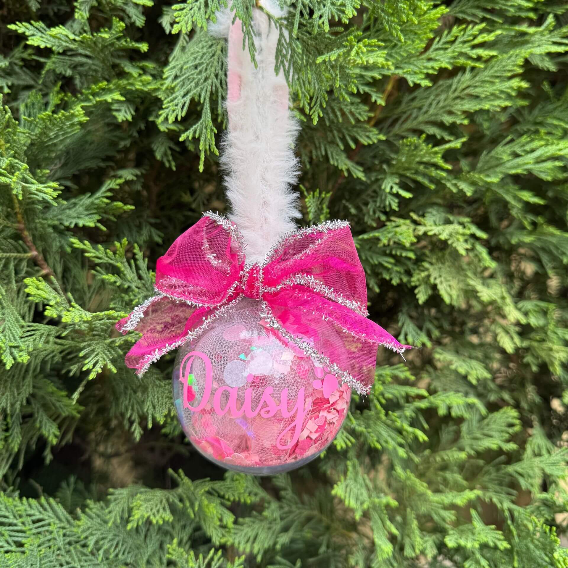 Pink ornament with a bow hanging on a Christmas tree