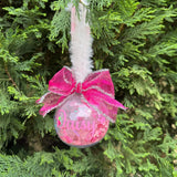 Pink ornament with a bow hanging on a Christmas tree