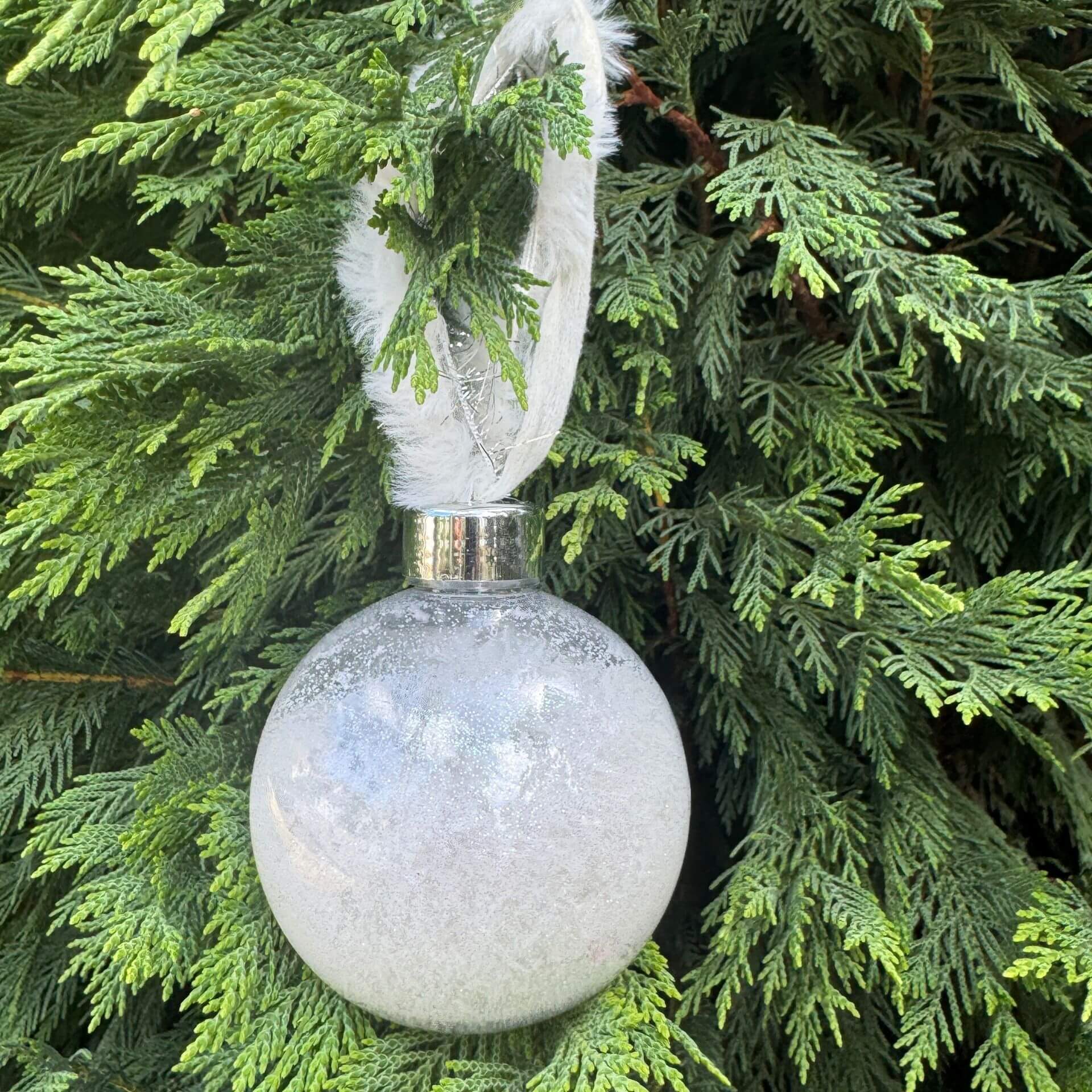Decorative white ornament with feather on a green tree